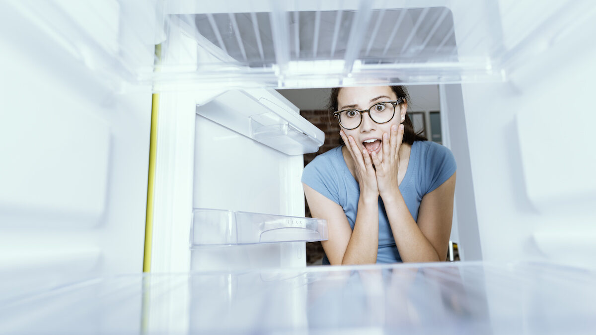 Женщина заглядывает в пустой холодильник